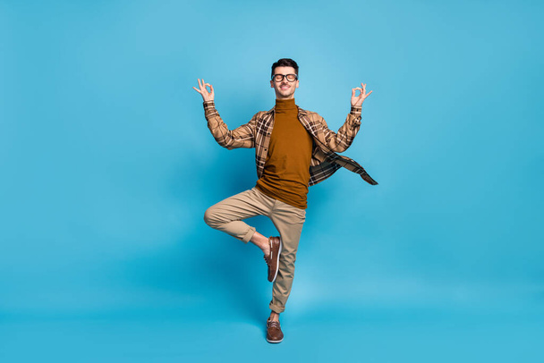 Full size photo of young funky funny smiling positive man doing yoga showing okay sign isolated on blue color background - Фото, зображення