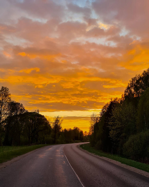 Aszfalt út a vidéken a narancssárga naplementében. A zöld tavaszi virágzó fák mellett. - Fotó, kép
