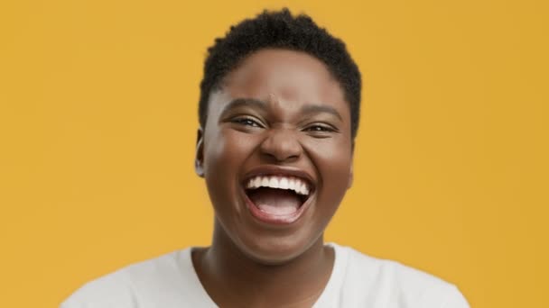 Femmina nera che ride ad alta voce guardando la fotocamera, sfondo giallo - Filmati, video
