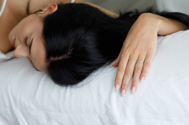Mujer joven agotada se desmayó durmiendo en un sofá blanco o en la cama de cerca en su mano y la parte superior de su cabeza con copyspace - Foto, imagen