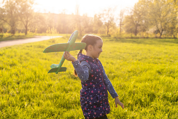 手におもちゃの飛行機を持つ女の子屋外、ゴムモーターのネジ風スティック - 写真・画像