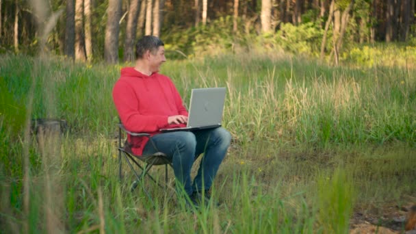 Lustiger Programmierer arbeitet im Sommerwald am Laptop - Filmmaterial, Video