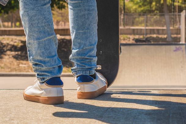 Detail záběr nohou nepoznatelného teenagerského bruslaře, který se připravuje jít po překážce v skate parku se svým skateboardem. - Fotografie, Obrázek