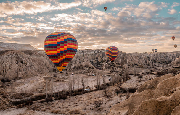 Goreme, Turkey - March 19, 2021 - Panorama view of hot air balloons flying in Cappadocia, Turkey at sunrise with rock formations and fairy chimneys - Photo, image