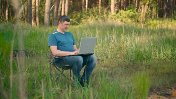 Сумасшедший программист работает на ноутбуке в летнем лесу - Кадры, видео