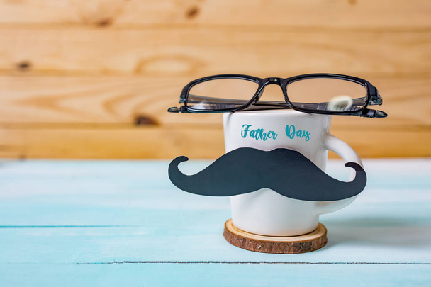 Happy Father's day concept. A black mustache paper, a cup of coffee and glasses on wooden table. - Фото, изображение
