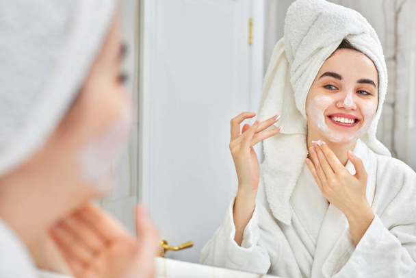 mujer en batas blancas aplicando aplicar crema facial - Foto, imagen