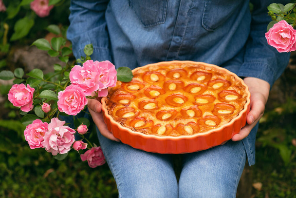 Домашний вкусный абрикосовый пирог с миндальными орехами в женских руках в летнем саду. Концепция сладкого. - Фото, изображение