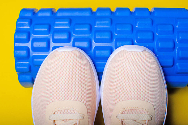Peach sneakers and a massage roller on yellow background. - Foto, immagini