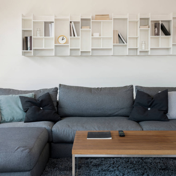 Moderni valkoinen hylly kirjoja ja koristeita yläpuolella mukava, harmaa kulma sohva - Valokuva, kuva