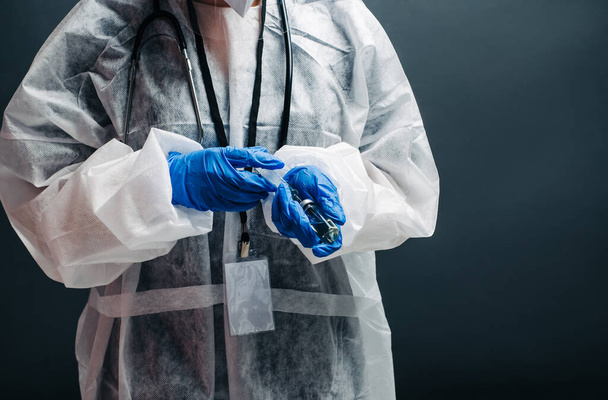 Gezondheidswerker in beschermende kleding en handschoenen met een injectiespuit en een injectieflaconvaccin, die wordt gevuld met covid-19-vaccin. Close-up - Foto, afbeelding