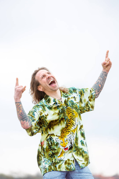 portrait of handsome young man with long hair screaming and making hand sign - Foto, immagini