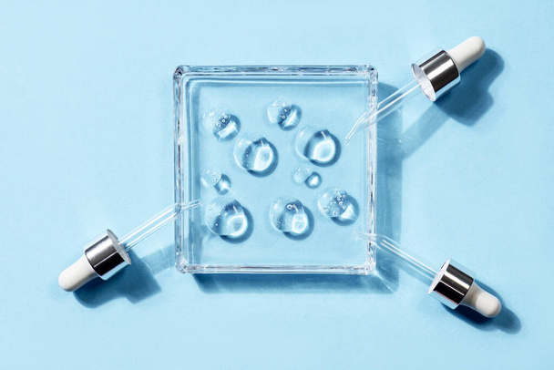Pipettes with drops of different forms of hyaluronic acid on a glass stand, blue background. Cosmetics concept - Φωτογραφία, εικόνα