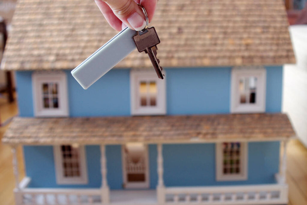 srebrny klucz z białym znaczkiem wiszącym przed dużym niebieskim drewnianym domkiem dla lalek  - Zdjęcie, obraz