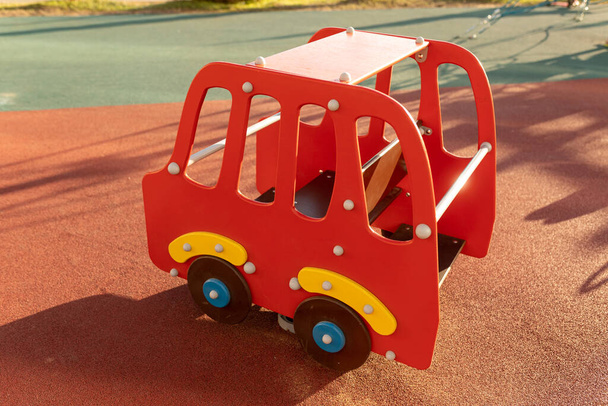 Ξύλινο παιδικό αυτοκίνητο στην παιδική χαρά. Swing με τη μορφή ενός αυτοκινήτου σε μια μαλακή κοκκώδη επιφάνεια από καουτσούκ της παιδικής χαράς - Φωτογραφία, εικόνα