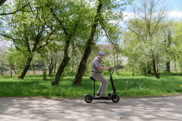 Un anciano positivo y carismático monta un eco scooter en el parque. Caminar en la naturaleza. El estilo de vida saludable de los ancianos. - Foto, imagen
