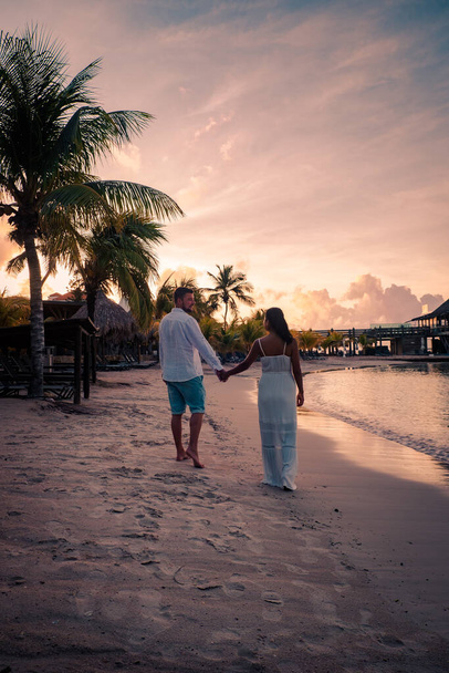 夕暮れ時のキュラソー島のビーチでカップル、男性と女性はキュラソー島の熱帯ビーチで夕日を見ます - 写真・画像