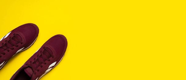 Пара бургундських чоловічих кросівок на жовтому тлі. Спортивне взуття, взуття для тренувань з фітнесу. Мінімалістичний фон з кросівками. Концепція здорового способу життя Плоский простір для копіювання зверху
. - Фото, зображення
