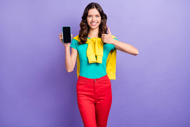 Portrait of lovely cheerful wavy-haired girl holding in hand device showing thumbup recommend isolated over violet pastel color background - Zdjęcie, obraz