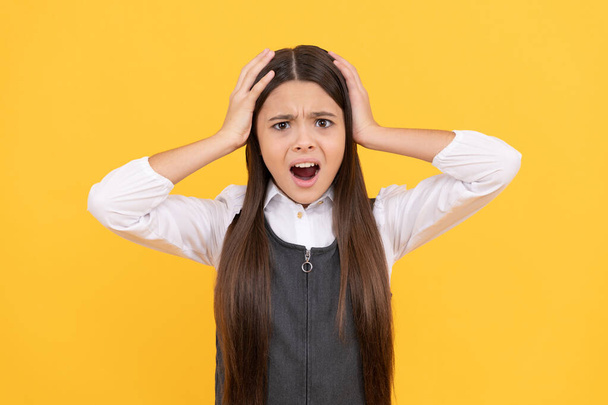 Shocked adolescente chica en uniforme escolar tomar la cabeza en las manos fondo amarillo, choque. - Foto, Imagen