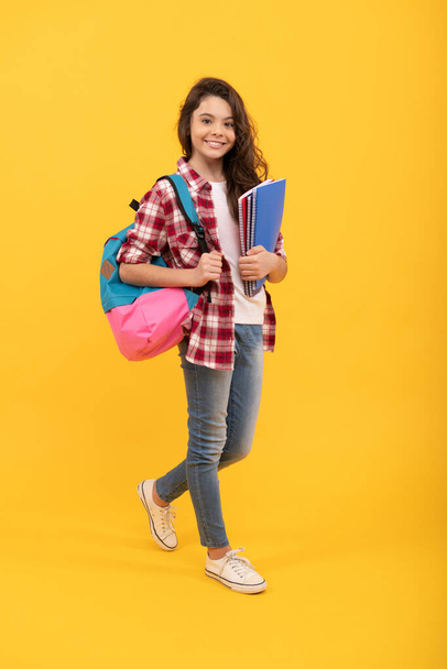 Fille heureuse de retour à l'école portant des livres et sac à dos fond jaune, école. - Photo, image