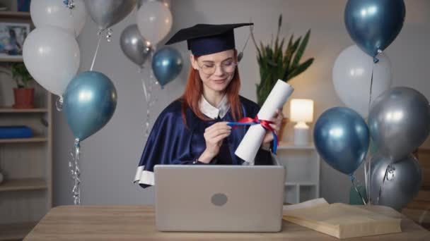 distance education, cheerful female student in academic dress at online graduation ceremony sits at home - Footage, Video
