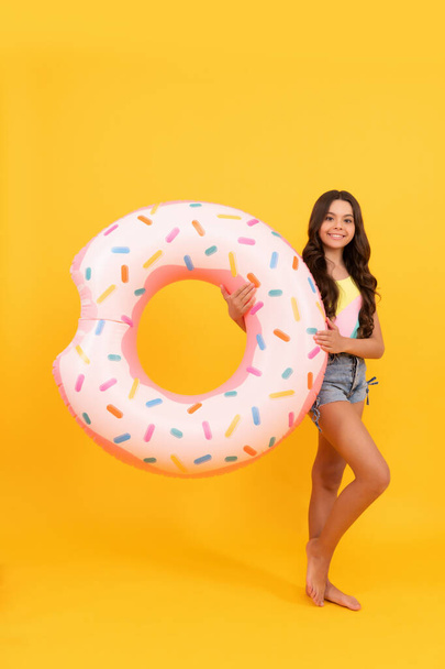 gelukkig strand tiener meisje met krullend haar met donut opblaasbare ring voor zwembad partij plezier op zomervakantie op gele achtergrond, zomertijd. - Foto, afbeelding