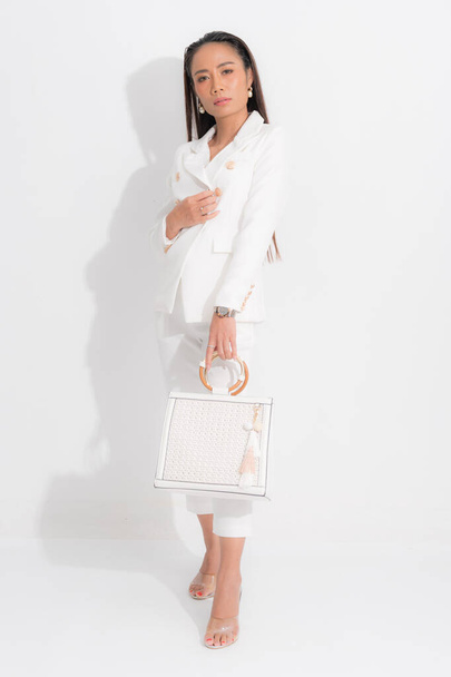 Μόδα στυλ κατάλογο ρούχα για τις επιχειρήσεις γυναίκα μαύρα μακριά μαλλιά φυσικό συνθέτουν φορούν λευκό κοστούμι κοστούμι τέλειο κοστούμι σώμα σχήμα, μεταφέρουν λευκή τσάντα στο στούντιο πυροβολούν σε λευκό φόντο και σκιά. - Φωτογραφία, εικόνα