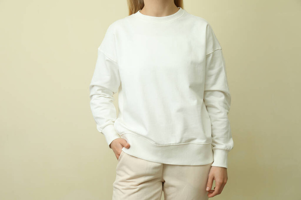 Young woman in white sweatshirt against beige background - Fotoğraf, Görsel