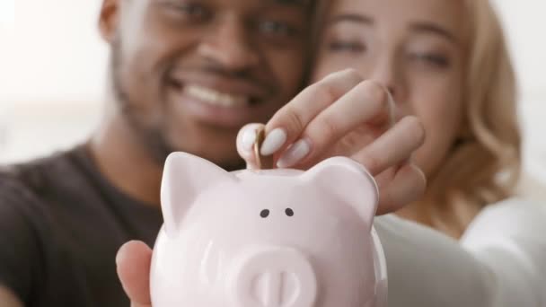 Oszczędności rodzinne, Szczęśliwa Para Wielorasowych Umieszczenie Monety w Piggybank w pomieszczeniach - Materiał filmowy, wideo