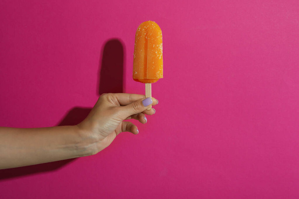 Nainen käsi pidä jäätelöä kiinni vaaleanpunainen tausta - Valokuva, kuva