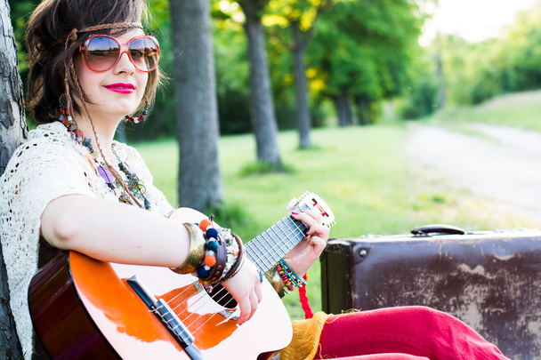 νεαρή γυναίκα που κάθεται σε ένα πεδίο και να παίζει κιθάρα - Φωτογραφία, εικόνα