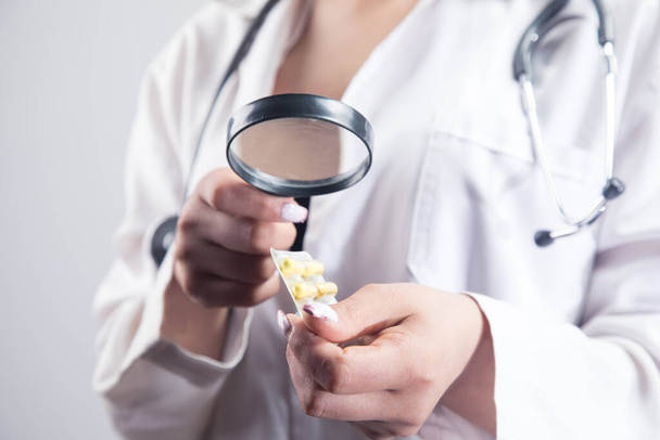 医者は虫眼鏡で薬を見てる。灰色の背景での薬物探索の概念 - 写真・画像