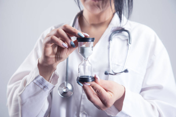 ženský lékař drží přesýpací hodiny na šedém pozadí - Fotografie, Obrázek