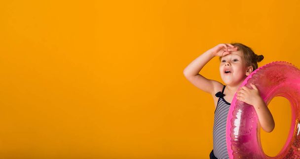 ritratto di una ragazza bionda felice in costume da bagno a righe che tiene un cerchio gonfiabile rosa su uno sfondo giallo con spazio per il testo. Sfondo estivo - Foto, immagini