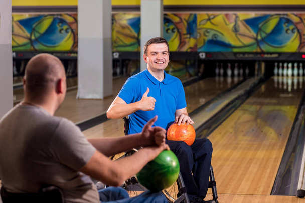 Two young disabled men in wheelchairs playing bowling in the club - Fotó, kép