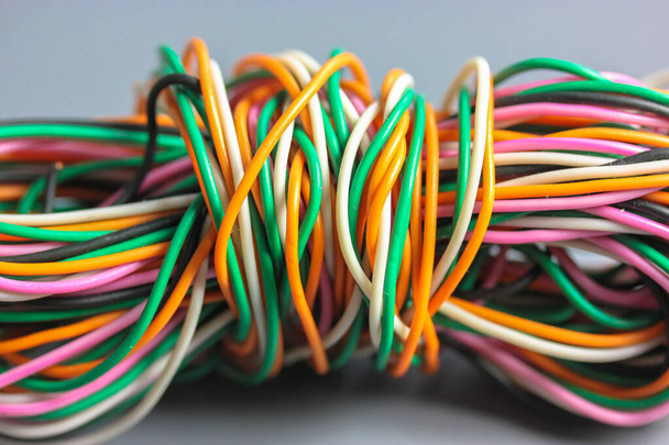 A bundle of multicolored electrical, car, computer, telephone wires twisted together background. Orange, green, pink, white cables on grey background . Computer networks, electrician services concept. - Photo, Image