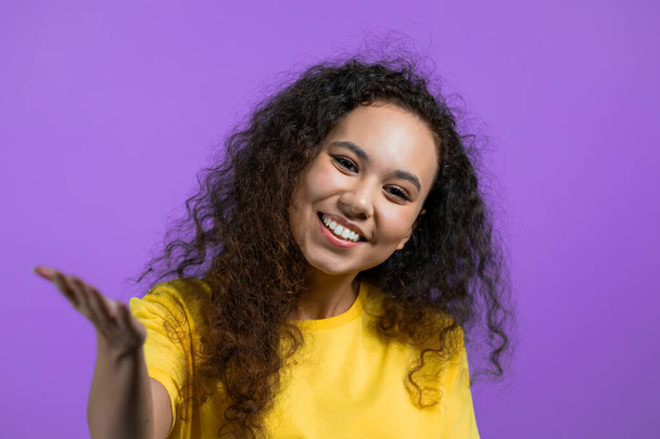 Beautiful woman showing - Hey you, come here. Girl in yellow ask join her, beckons with inviting hand hugs gesture. Lady is looking playful flirtatious, inviting to come. Violet studio background. - Photo, image