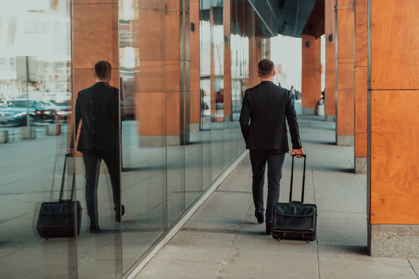 Going to the airport terminal. Young confident businessman traveler walking on city streets and pulling his suitcase drinking coffee and speaking on a smartphone. High quality photo - Foto, Imagem