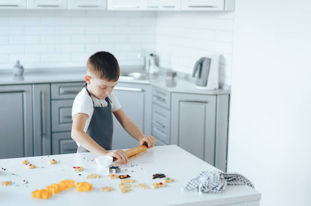 Boy in an apron rolls out the dough. Leisure activity with children concept. - Fotografie, Obrázek