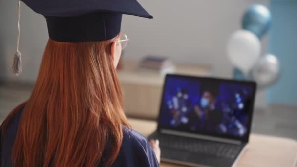 remote education, female student in an academic gown and hat receives a diploma at an online ceremony with male teacher in medical mask via video link on laptop - Video