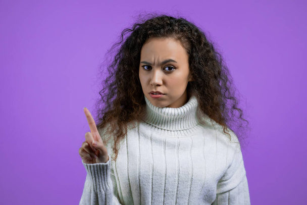 Portrait of serious woman showing rejecting gesture by stop finger sign. Girl in sweater isolated on violet background. - Фото, зображення