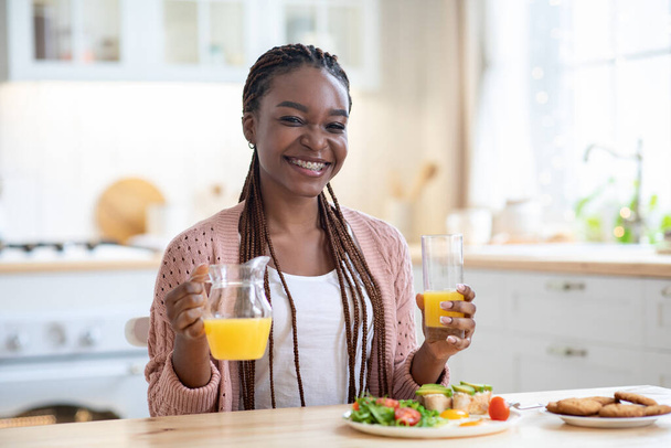 Desayuno en casa. Joven feliz dama negra teniendo sabrosa comida en la cocina - Foto, imagen