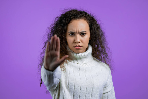 Pretty woman disapproving with NO hand sign gesture. Denying, rejecting, disagree, portrait of beautiful girl with curly hair on violet background - Foto, Imagem