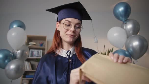 emotionaalinen tyttö akateemisessa puvussa iloitsee yliopistotutkinnon saamisesta verkossa ja puhuu videopuhelulla kannettavalla tietokoneella sosiaalisen etäisyyden ja etäopetuksen aikana - Materiaali, video