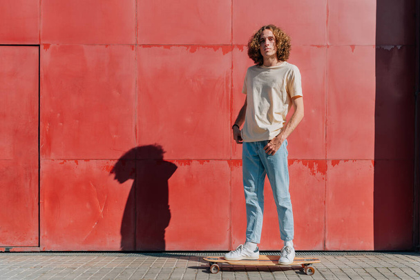 Горизонтальный портрет привлекательного молодого человека, стоящего на скейтборде - Фото, изображение