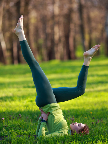 Athletic sportive girl in the park on green grass doing fitness exercises stretching the body, healthy lifestyle in pure nature - Фото, зображення