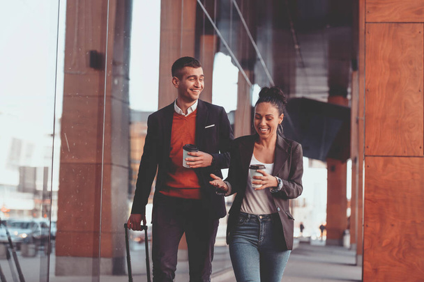Businessman and businesswoman talking and holding luggage traveling on a business trip, carrying fresh coffee in their hands. Business concept. High-quality photo - Foto, immagini