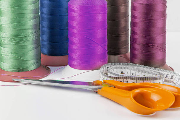 Colorful sewing threads, tailor's scissors and measuring tape in the foreground - Photo, Image