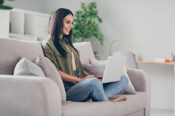 Full body profile side photo of young woman happy positive smile sit couch look browse laptop indoors - Fotoğraf, Görsel